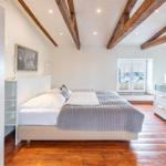 Bedroom with wooden floor, exposed beams, window, and white bed.
