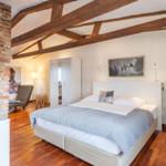 Bedroom with wooden beam ceiling, bed, wardrobe, and hardwood floor.