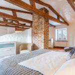 Bedroom with wooden beam ceiling, brick pillar, and bed with gray quilt.