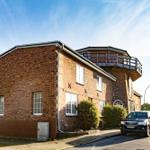 Red brick house with balcony and windows, parked cars in front of the facade.