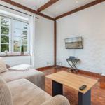 Living room with sofa, TV, and wooden floor. Window with view of garden.