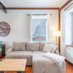 Living room with sofa, table, and wall clock. Wooden windows and beams.