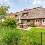 Red brick house with thatched roof and garden area with table and chairs.