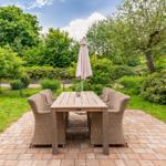 Garden with table, four chairs, and closed umbrella on stone paving.