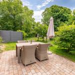 Terrace with table and chairs, surrounded by greenery and a closed parasol.