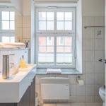 Badezimmer mit Waschbecken, Toilette und Fenster mit Blick auf Gebäude.