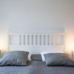 Ein Bett mit grauer Bettwäsche und zwei Nachttischen mit Lampen.