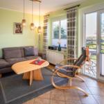 Wohnzimmer mit Sofa, Tisch und Sessel. Durchgang zur Terrasse mit Blick auf Feld.