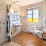 Badezimmer mit Dusche, Waschbecken und WC. Fenster mit gelben Jalousien.