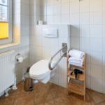Badezimmer mit WC, Handtuchständer und Fenster mit Jalousie.