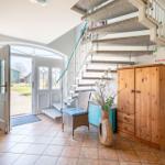 Eingangsbereich mit Treppe, Holzschränken und Glastür zur Außenterrasse.