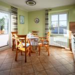 Essbereich mit Tisch, Stühlen und Küchenzeile. Durchgänge zu Terrasse und Fenster.