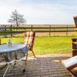 Terrasse mit Tisch, zwei Stühlen und Strandkorb. Blick auf grünes Feld und Holzzaun.