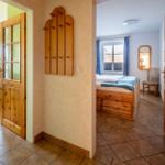 Schlafzimmer mit Holzbett und Fenster. Flur mit Holztür und Wandgarderobe. Wohnbereich mit Tisch und Stühlen.