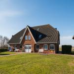 Red brick house with dormers and white front door. Lawn and wooden building to the right.