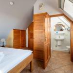 Bedroom with sloped ceiling, wooden bed, wardrobe, and adjacent toilet cubicle.