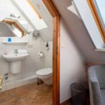 Bathroom with toilet, sink, and skylight. Adjacent area with seating.
