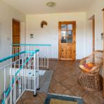 Entrance area with bookcase, wicker chair, and blue handrail.