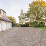 Haus mit Kiesfläche, Grünflächen und Bäumen im Herbstlicht.