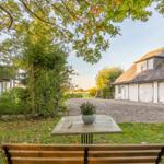 Ein Tisch und Stuhl im Garten vor einem weißen Haus mit Schopf und Garage.