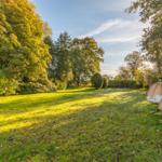 Großer Garten mit Grasfläche, Bäumen und zwei hängenden Sitzmöbeln.