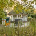 Ein weißes Haus mit strohgedecktem Dach und großem Fensterbereich im Garten.