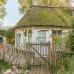 Ein kleines Haus mit Strohdach, umgeben von Grün und einem Holzzaun.