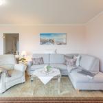 Wohnzimmer mit Ecksofa, Sessel, Glas-Tisch und Wandbild.