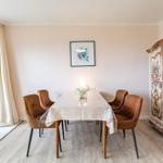 Esszimmer mit Tisch, vier Stühlen, Wandbild und dekorativem Schrank.