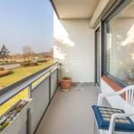 Balkon mit Stuhl, Pflanze und Blick auf Grünfläche und Straße.