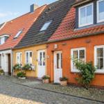 Reihenhaus mit rotem Dach und farbigen Fassaden an einer Kopfsteinpflasterstraße.