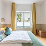 Schlafzimmer mit Bett, Fenster und gelben Vorhängen. Holzboden und Schrank.