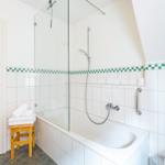 Badezimmer mit Badewanne, Dusche und Toilette. Weiße Fliesen mit grüner Zierleiste.