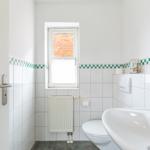Badezimmer mit Toilette, Waschbecken und Fenster mit Blick auf Backsteinmauer.