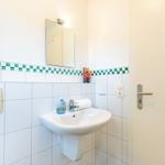 Badezimmer mit Waschbecken, Spiegel und grüner Fliesendekoration an der Wand.