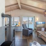 Wohnzimmer mit Holzdecke, Kamin, Sofa und TV. Blick auf Terrasse und Strand.