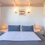 Schlafzimmer mit Bett, Nachttischen und Wandbild. Holzdecke und warme Beleuchtung.