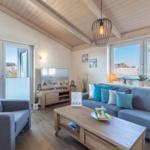 Wohnzimmer mit Sofa, Sessel und TV. Holzdecke und große Fenster.