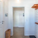 Eingangsbereich mit Garderobe, Korb und Tür. Holzboden und weiße Wände.