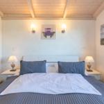 Schlafzimmer mit Bett, Nachttischen und Wandbildern. Holzdecke und Lampen.