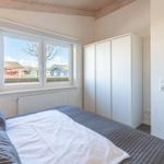 Schlafzimmer mit Bett, Kleiderschrank und Fensterblick auf Häuser.