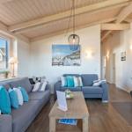 Wohnzimmer mit zwei Sofas, Holzdecke und Kaminofen. Fenster blicken auf Wohnhaus.