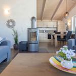 Wohnzimmer mit Kamin, Essbereich und Küche im Hintergrund. Holzdecke und moderne Einrichtung.