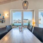 Esszimmer mit langem Holztisch, schwarzen Stühlen und Fensterblick auf Außenbereich.
