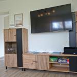 Wohnzimmer mit TV, Holzmöbel und Regalen. Flur und Tür sind sichtbar.