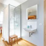 Bathroom with shower, sink, and mirror. Wooden floor and door.
