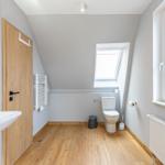 Bathroom with toilet, sink, and wooden floor. Windows provide natural light.