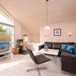 Wohnzimmer mit Sofa, Fernseher und Kamin. Große Fenster und Holzwände.