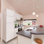 Moderne Küche mit weißen Schränken, dunklem Arbeitsplatz und Holzwandverkleidung.