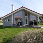 Moderne Holzhütte mit Terrasse, Garten und Sitzgelegenheiten.